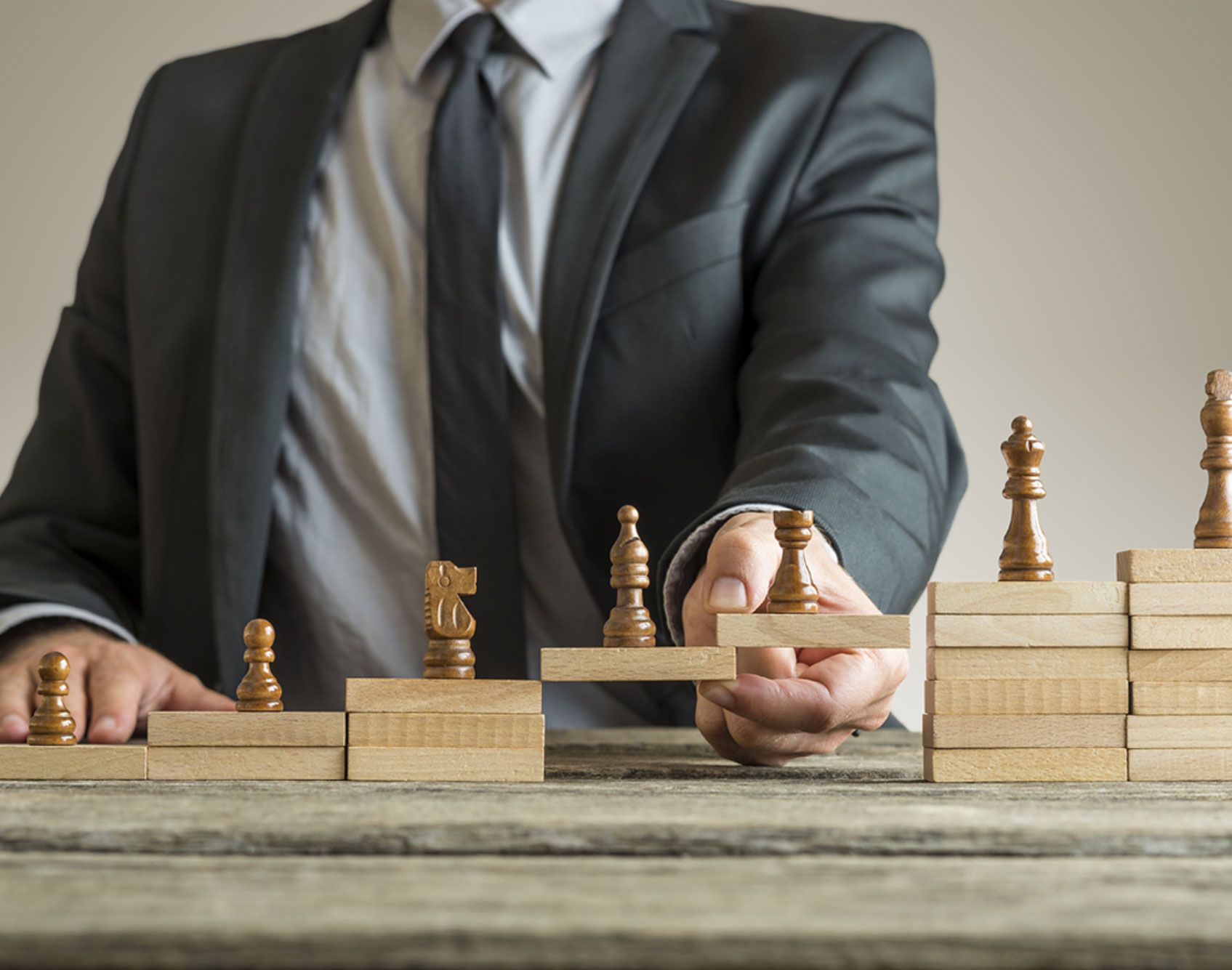 Business professional in suit arranging wooden chess pieces on stacked blocks, symbolizing strategic growth and decision-making.