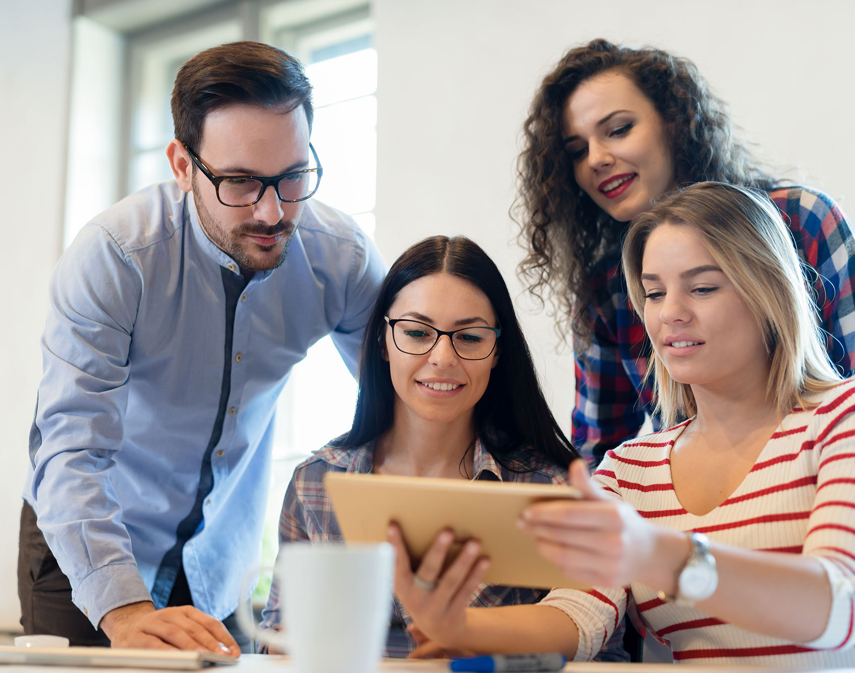 Group of diverse coworkers collaborating in an office, analyzing data on a tablet, emphasizing teamwork and innovative strategies for growth in mission-driven organizations.