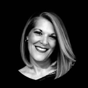 Smiling woman with shoulder-length hair, wearing a black top, representing Stratica AX, a consulting firm focused on growth leadership for mission-driven organizations.