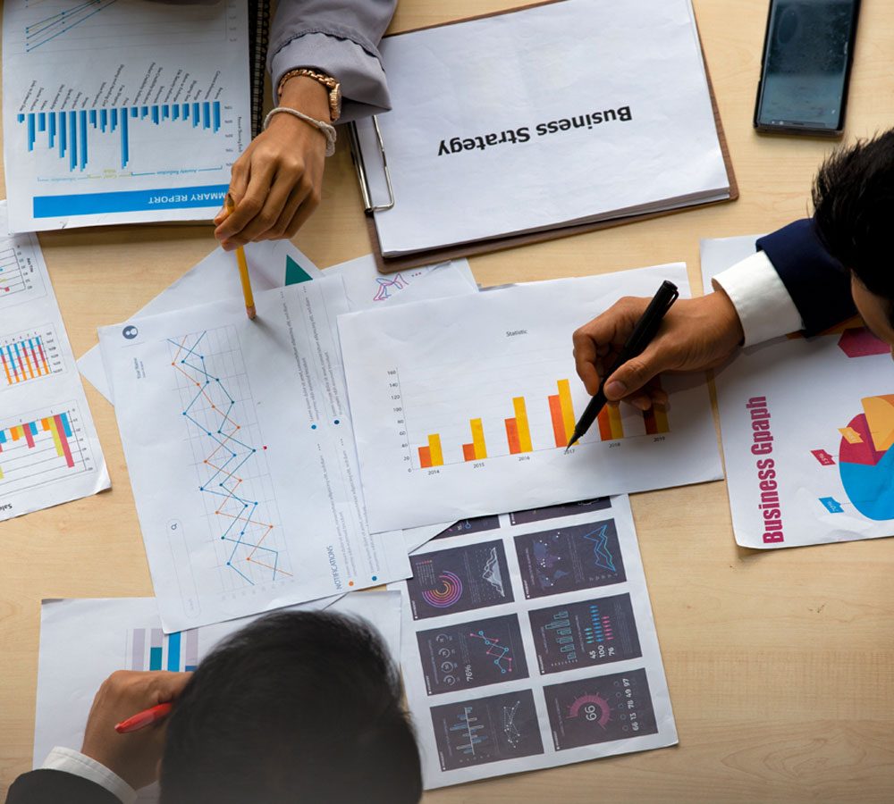 Hands analyzing business strategy documents, including various graphs and charts, emphasizing market analysis and growth metrics for strategic planning.