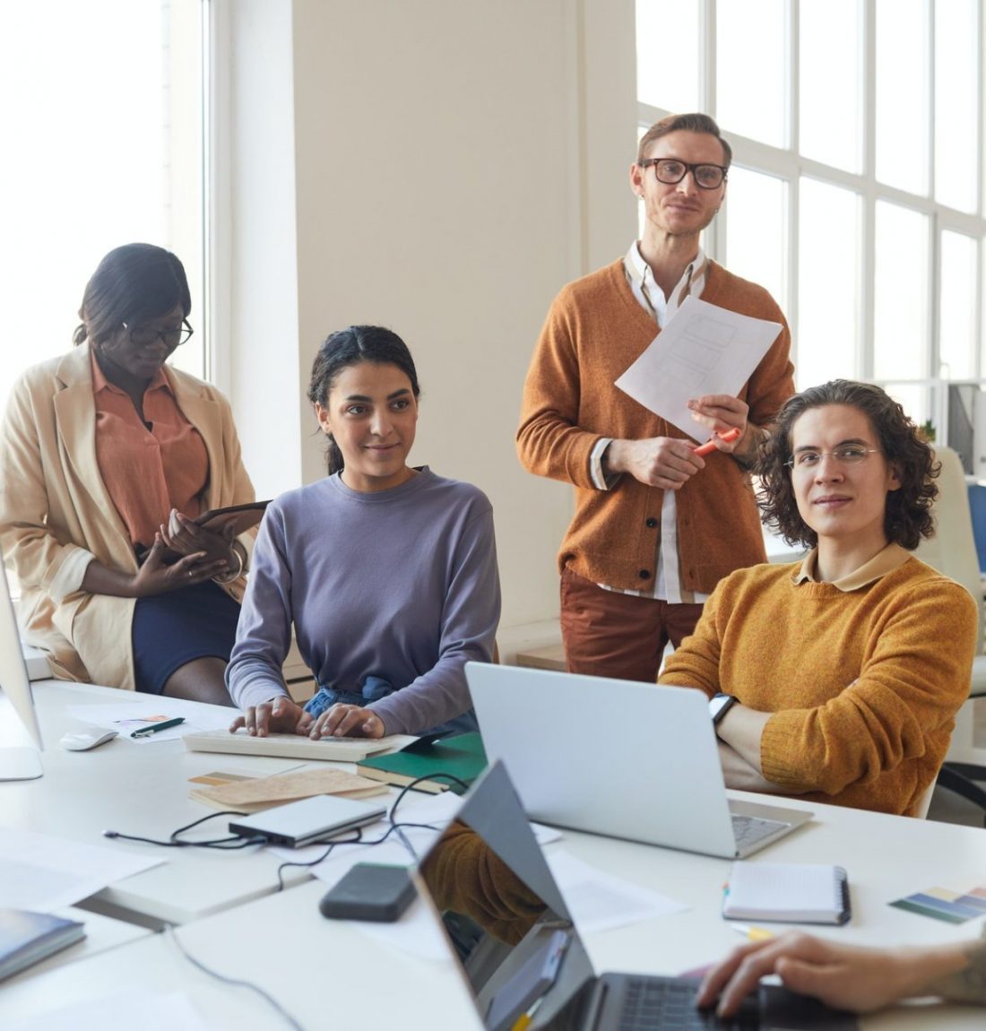 Creative IT development team collaborating in a modern office, featuring diverse professionals engaged in strategy discussions and planning, with laptops and documents on a table.